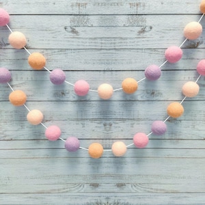 Mädchenhafte Girlande in Pfirsich, Rosabeige, Kirschrosa und Mauve, aus Filzkugeln, Merinowolle. Pastellfarbene Pompon-Girlande für das Babyzimmer eines Mädchens.