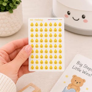May include: A rectangular sticker sheet featuring rows of small yellow water drop icons with smiling faces. The text PEE TRAINING and EMPIRESTICKERPLANNER is printed at the top. The stickers are designed for potty training progress tracking.