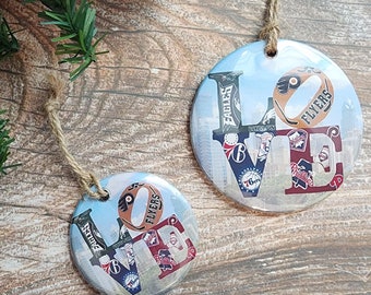May include: Two round, silver ornaments with a collage of Philadelphia sports team logos forming the word "LOVE". The ornaments are hanging from twine.