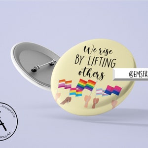 May include: A yellow button with the text "We rise by lifting others" and a variety of pride flags held by hands of different skin tones. The text "@EMSFABULOUSART" is in the bottom right corner.