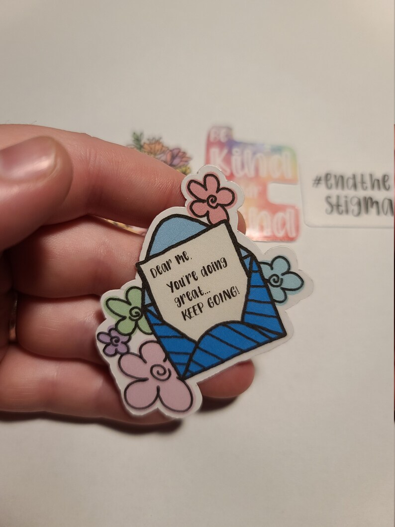 May include: A blue and white envelope sticker with the text "Dear me. You're doing great... KEEP GOING!" surrounded by pink, green, and purple flowers.