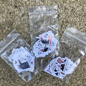 K&ouml;nnte beinhalten: Drei transparente Plastikt&uuml;ten voller Aufkleber. Jeder Aufkleber zeigt einen Mann in Anzug und Krawatte mit dem Text "I DID THAT!" und Sternen. Die T&uuml;ten liegen auf einer strukturierten, grauen Oberfl&auml;che.