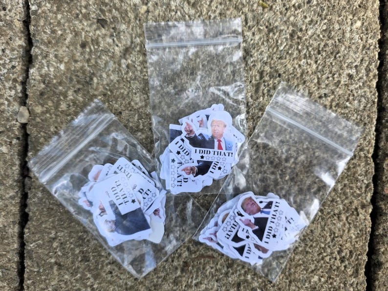 K&ouml;nnte beinhalten: Drei transparente Plastikt&uuml;ten voller Aufkleber. Jeder Aufkleber zeigt einen Mann in Anzug und Krawatte mit dem Text "I DID THAT!" und Sternen. Die T&uuml;ten liegen auf einer strukturierten, grauen Oberfl&auml;che.