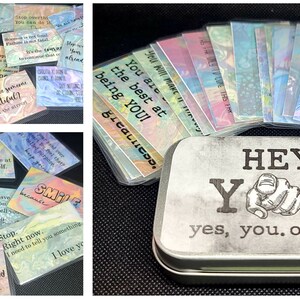 May include: A silver tin with the words "HEY YOU! yes, you. open me." printed on it. The tin contains a set of colorful cards with positive affirmations, such as "You are the best at being YOU!" and "Life is short. Too short. Stop wasting time at war with yourself."