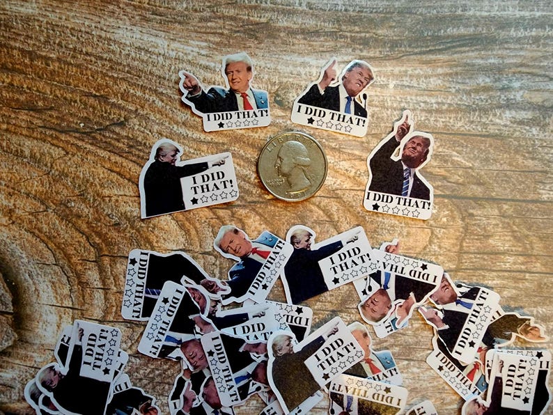 K&ouml;nnte beinhalten: Eine Sammlung von Aufklebern mit einem Mann im Anzug mit dem Text "I DID THAT!" und einer Sternebewertung. Ein US-Vierteldollar ist ebenfalls vorhanden. Die Aufkleber sind auf einer Holzoberfl&auml;che verstreut.