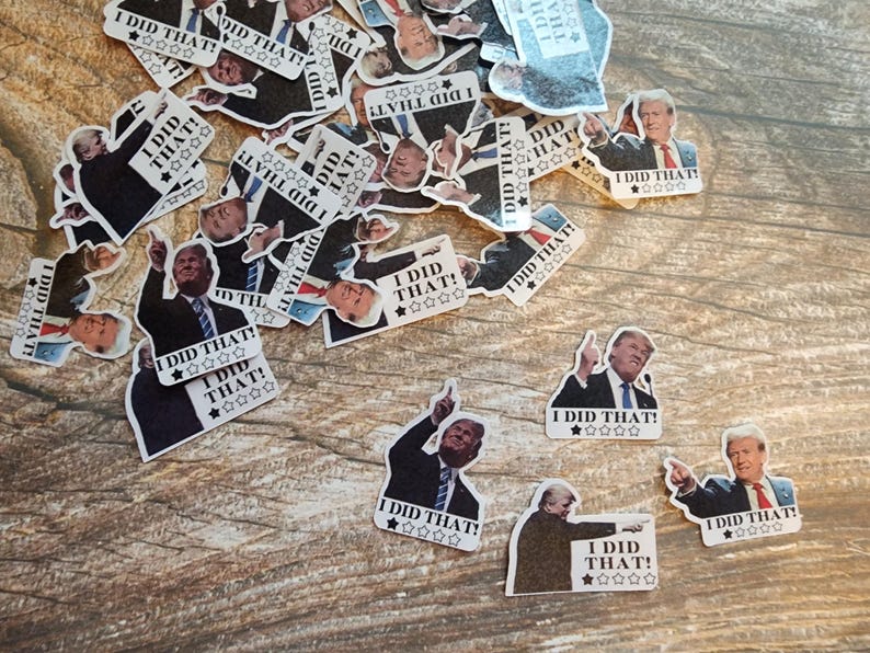 K&ouml;nnte beinhalten: Eine Ansammlung von Aufklebern mit einem Mann im Anzug und dem Text "I DID THAT!" sowie Sterngrafiken. Die Aufkleber sind auf einer Holzoberfl&auml;che verteilt.