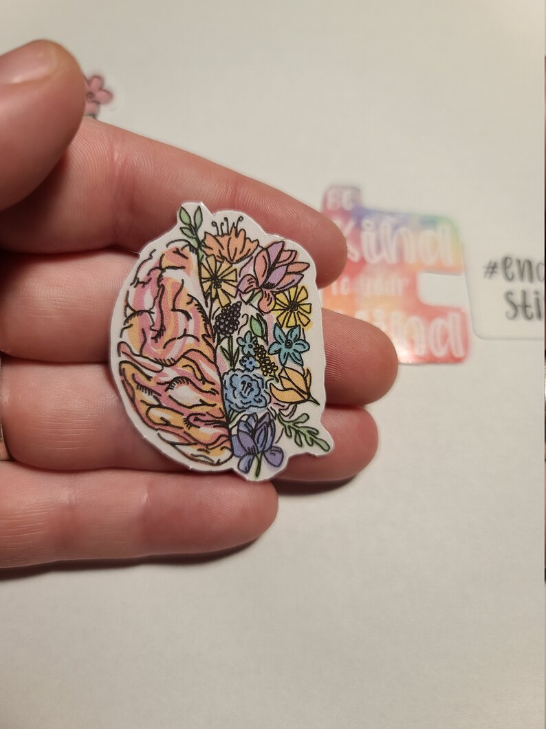 May include: A sticker featuring a colorful floral design inside a pink brain outline. The sticker is on a white background.