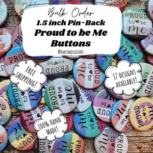 May include: A close-up of a collection of 1.5 inch pin-back buttons with the text "Proud to be Me" and various rainbow pride flag designs. The buttons are arranged in a random pattern on a wooden surface. The text "Bulk Order" and "17 Designs Available!" are visible in the image.