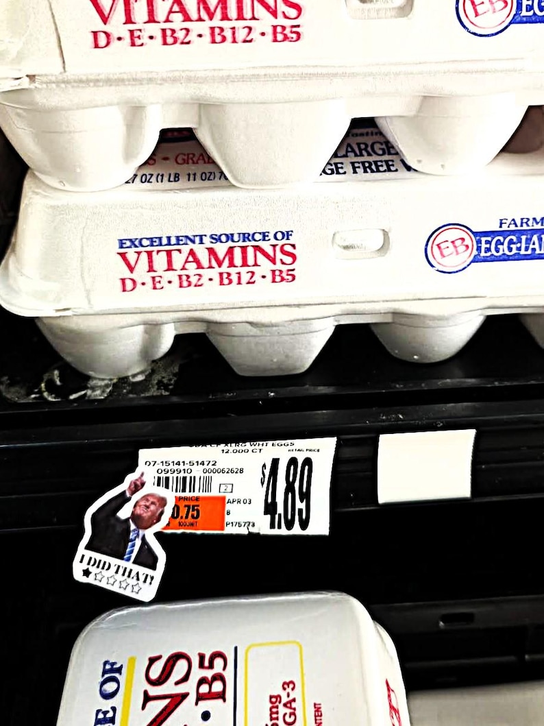 K&ouml;nnte beinhalten: Nahaufnahme von gestapelten wei&szlig;en Eierkartons mit dem Text "Excellent Source of Vitamins D-E-B2-B12-B5". Ein Aufkleber mit dem Text "I DID THAT!" befindet sich auf dem Regal unter den Kartons. Ein Preisschild zeigt den Preis von 4,89 $.