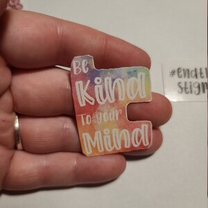 May include: A colorful sticker with the text "Be Kind To Your Mind" in white lettering on a rainbow watercolor background. The sticker is in the shape of a rectangle with rounded corners. The hashtag "#endthestigma" is visible in the background.