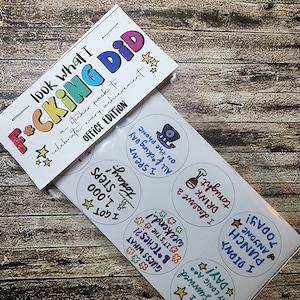 May include: A sticker pack with the text "look what I F*CKING DID" and "OFFICE EDITION". The pack includes round stickers with phrases like "I survived a long a** day!" and "I didn't punch anyone today!"