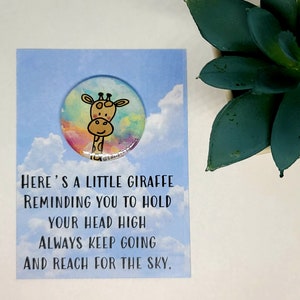 May include: A motivational card with a colorful giraffe illustration on a button. The card reads "Here's a little giraffe reminding you to hold your head high always keep going and reach for the sky."