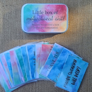 May include: A small metal tin with a watercolor design and the text "Little box of motivational shit! Because we all need a kick in the ass sometimes!"  The tin contains a stack of cards with watercolor designs and motivational phrases.