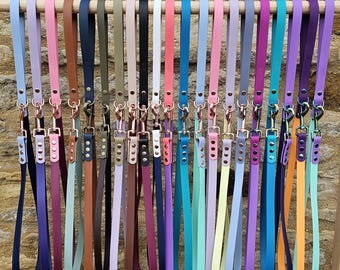 May include: A collection of 24 colorful leather dog leashes with rose gold hardware. The leashes are arranged in a row, hanging from a wooden dowel.