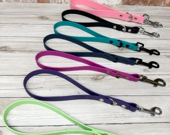 May include: A collection of six waterproof dog leashes in pink, black, teal, navy blue, magenta, purple, and lime green. Each leash features a loop handle, a metal D-ring, and a metal swivel snap hook attached with two rivets at the base.