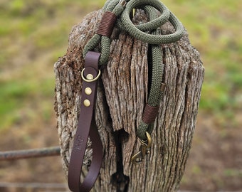 May include: A brown leather dog leash with a green rope leash attached. The leashes are tied around a weathered wooden post.