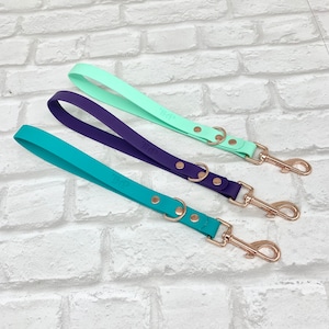 May include: Three short dog leashes in mint green, deep purple, and teal. Each leash features a smooth, flat strap with the embossed letters THP, secured by two metallic rivets, a circular metal ring, and a rose gold-toned swivel snap hook.