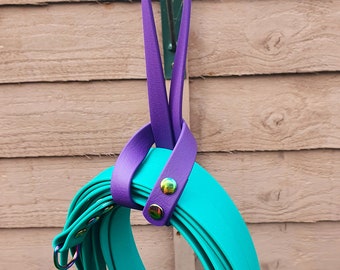 May include: A set of teal colored dog leashes with purple leather handles and iridescent metal hardware. The leashes are hanging on a hook.