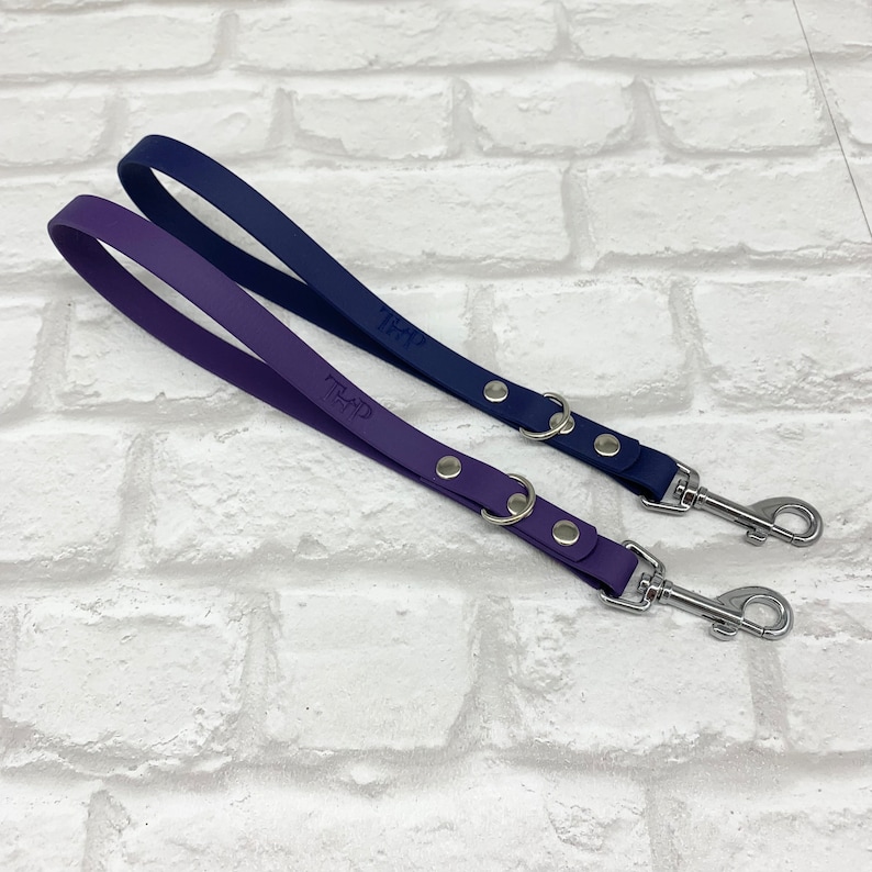 May include: Two dog leashes, one in purple and one in navy blue, featuring a smooth matte finish. Each leash includes a silver-toned metal swivel snap hook, a circular metal ring, and two silver rivets. The letters THP are embossed on each strap.