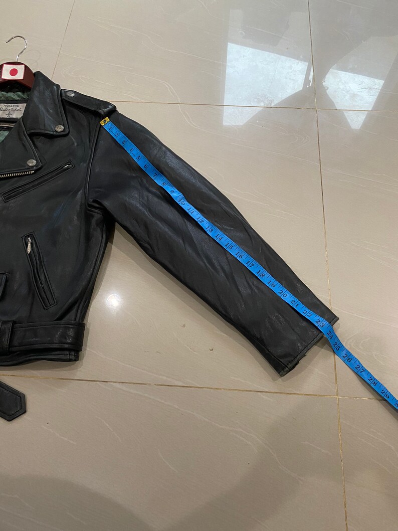 May include: Black leather motorcycle jacket with a zipper closure and a blue measuring tape showing the sleeve length is 28 inches.