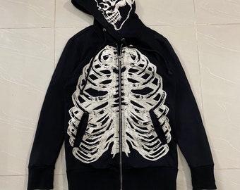 May include: Black zip-up hoodie with a white skeleton graphic on the front and a white skull graphic on the hood.