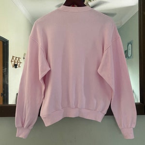 Puede incluir: Una sudadera de manga larga de color rosa p&aacute;lido con cuello redondo.