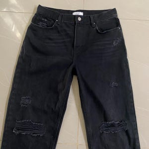 Puede incluir: Vaqueros negros desgastados de denim con m&uacute;ltiples roturas y desgarros en toda la tela.