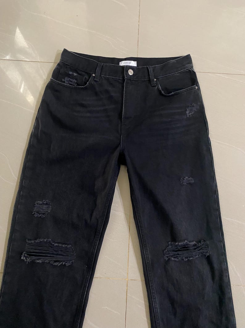 Puede incluir: Vaqueros negros desgastados de denim con m&uacute;ltiples roturas y desgarros en toda la tela.