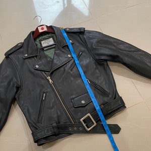 May include: Black leather motorcycle jacket with a zipper closure, two pockets, and a belt. The jacket is hanging on a hanger with a Japanese flag.