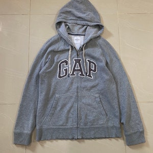 Könnte beinhalten: Ein grauer Kapuzenpullover mit Reißverschluss und dem Schriftzug "GAP" in weißer und schwarzer Schrift auf der Vorderseite.