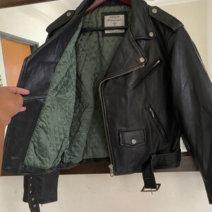 May include: Black leather motorcycle jacket with a green quilted lining. The jacket has a zipper closure, a belt, and a label that reads "Timeless Riders Jacket".