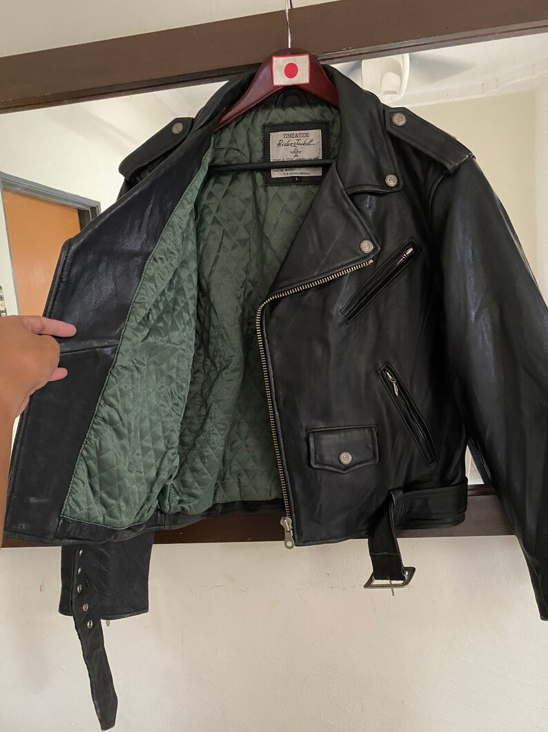 May include: Black leather motorcycle jacket with a green quilted lining. The jacket has a zipper closure, a belt, and a label that reads "Timeless Riders Jacket".