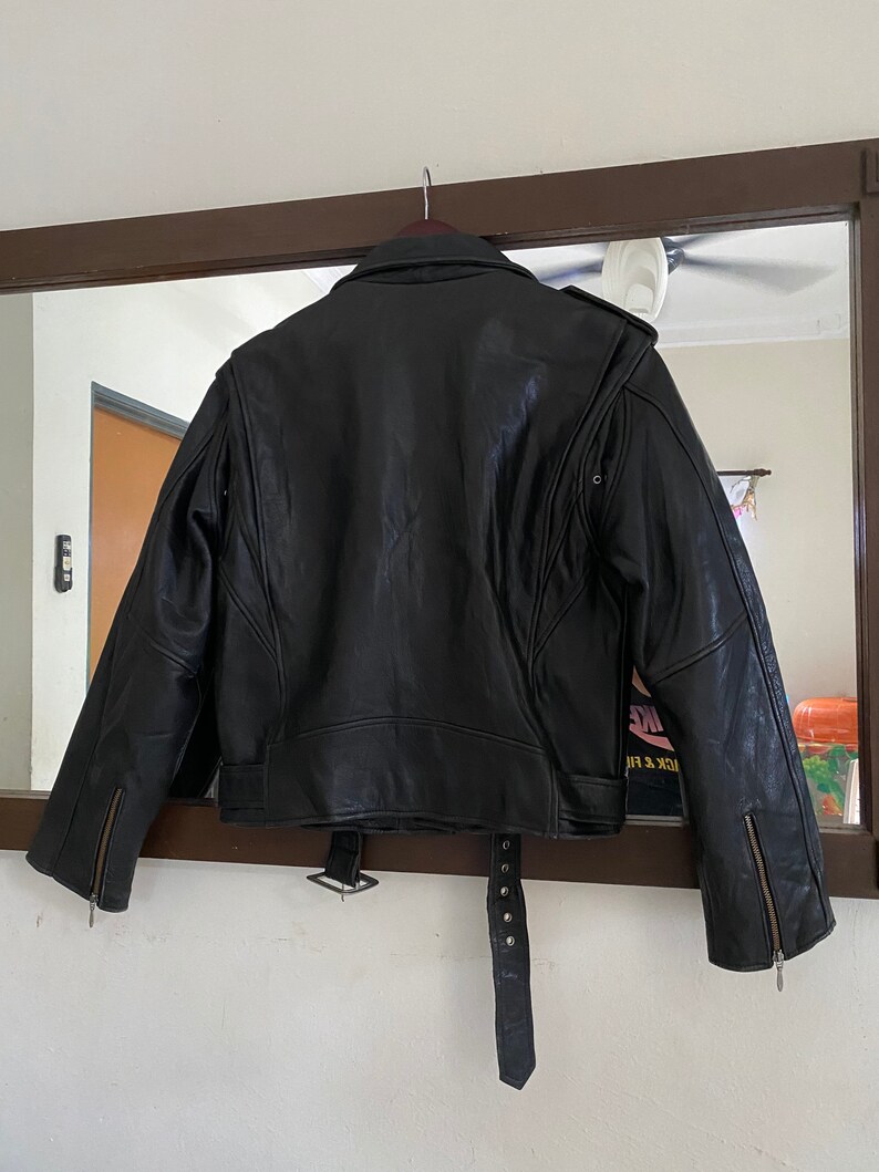 May include: Black leather jacket with a belt and zippered cuffs. The jacket has a classic biker style.