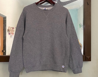 May include: A gray sweatshirt with a crew neck and long sleeves. The sweatshirt has a small logo on the left chest and a larger logo on the lower right side.