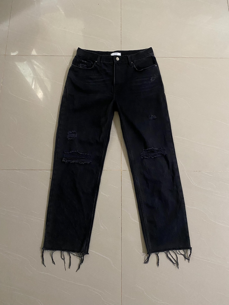 Puede incluir: Vaqueros negros desgastados de denim con dobladillos deshilachados.