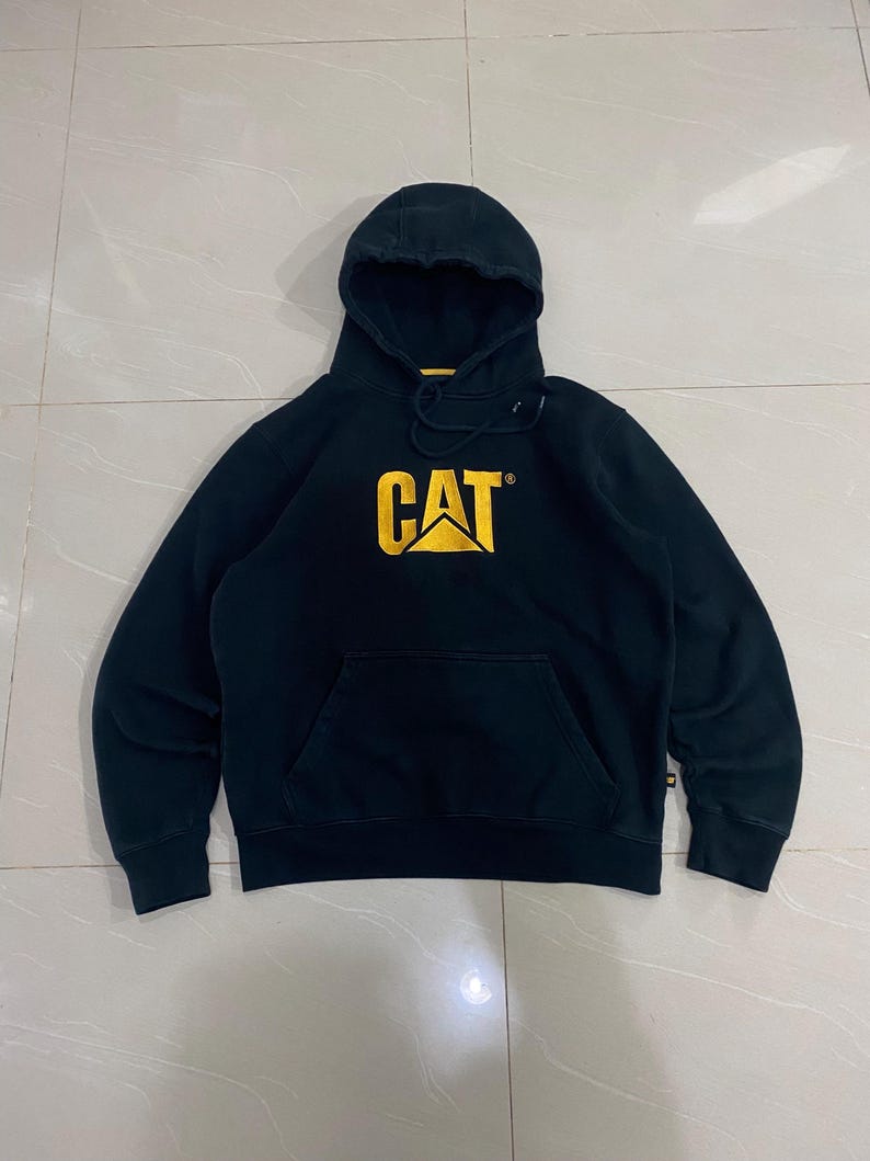May include: Black hooded sweatshirt with a kangaroo pocket and the CAT logo in yellow. The sweatshirt has a drawstring hood and long sleeves. The CAT logo is centered on the chest.
