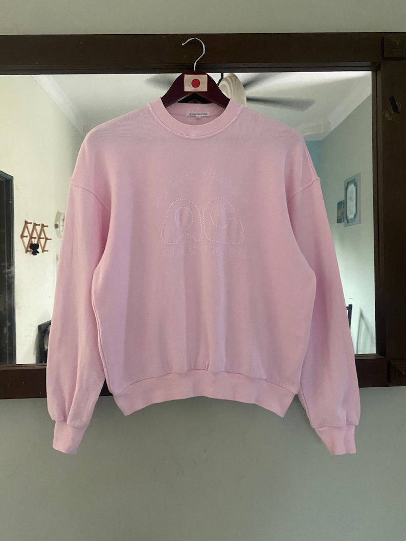 Puede incluir: Una sudadera rosa con un logotipo bordado en blanco que dice "A Cold Wall*" y tiene un dise&ntilde;o de nube.