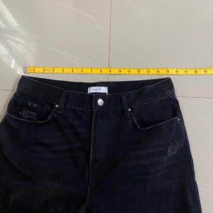 Puede incluir: Vaqueros de denim negro desgastados con una cintura de 38 cm.
