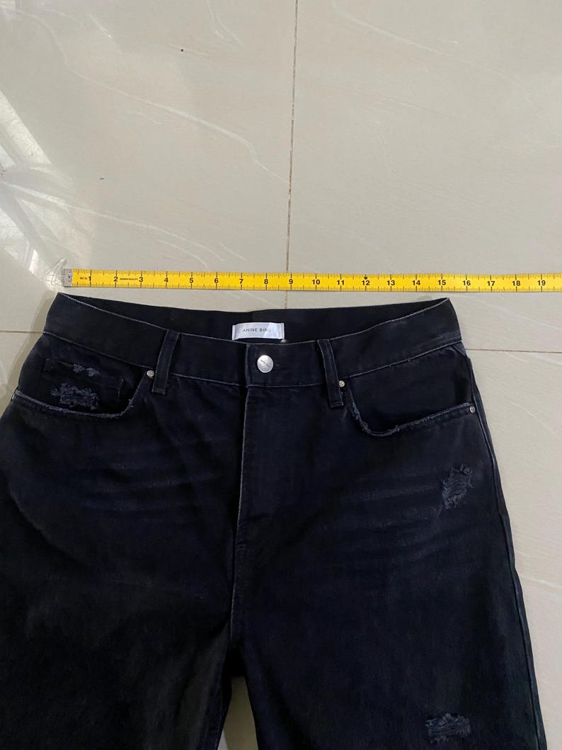 Puede incluir: Vaqueros de denim negro desgastados con una cintura de 38 cm.
