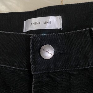 Puede incluir: Vaqueros negros de denim con una etiqueta blanca que dice "Anine Bing" y un bot&oacute;n plateado con el mismo texto.