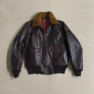 May include: A brown leather bomber jacket with a fur collar. The jacket has a zipper closure, two front pockets, and ribbed cuffs and hem. The interior lining is red.