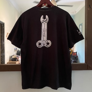 Könnte beinhalten: Schwarzes T-Shirt mit einem weißen Schraubenschlüssel-Motiv und dem Wort "TOOL" auf der Rückseite.