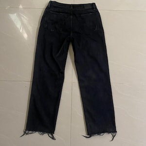 Puede incluir: Vaqueros de mezclilla negra con dobladillo deshilachado. Los vaqueros tienen un corte holgado y una pierna recta.