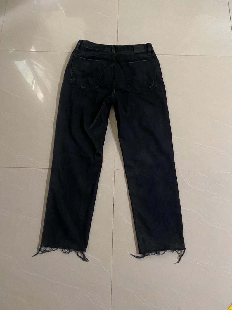 Puede incluir: Vaqueros de mezclilla negra con dobladillo deshilachado. Los vaqueros tienen un corte holgado y una pierna recta.