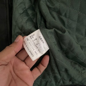 May include: A white tag with black text that reads "品質表示 番:TJKB006 表地:牛革 裏地:ポリエステル 100% 中綿:ポリエステル 100% MADE IN PHILIPPINES".
