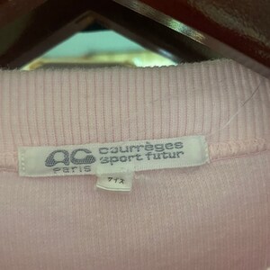 Puede incluir: Una camiseta de punto de canal&eacute; rosa con una etiqueta blanca que dice "Courr&egrave;ges Sport Futur Paris" y "サイズ" en japon&eacute;s.