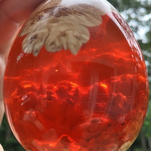 May include: A red and white resin egg with a swirling pattern inside. The egg is translucent and the pattern is visible through the resin.