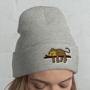 May include: A gray beanie with a brown monkey sleeping on a branch embroidered on the front.