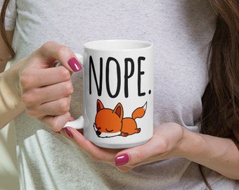 May include: White ceramic mug with a black and white graphic of a fox and the word "NOPE."