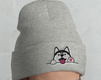 Könnte beinhalten: Eine graue Mütze mit einem schwarz-weißen Husky-Hund, der hinter dem Rand hervorlugt. Der Hund hat eine rosa Zunge herausgestreckt und einen Pfotenabdruck an der Seite des Kopfes.